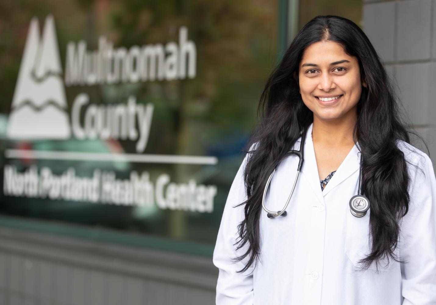 A doctor with a stethoscope around her neck stands outside the North Portland Health Center.