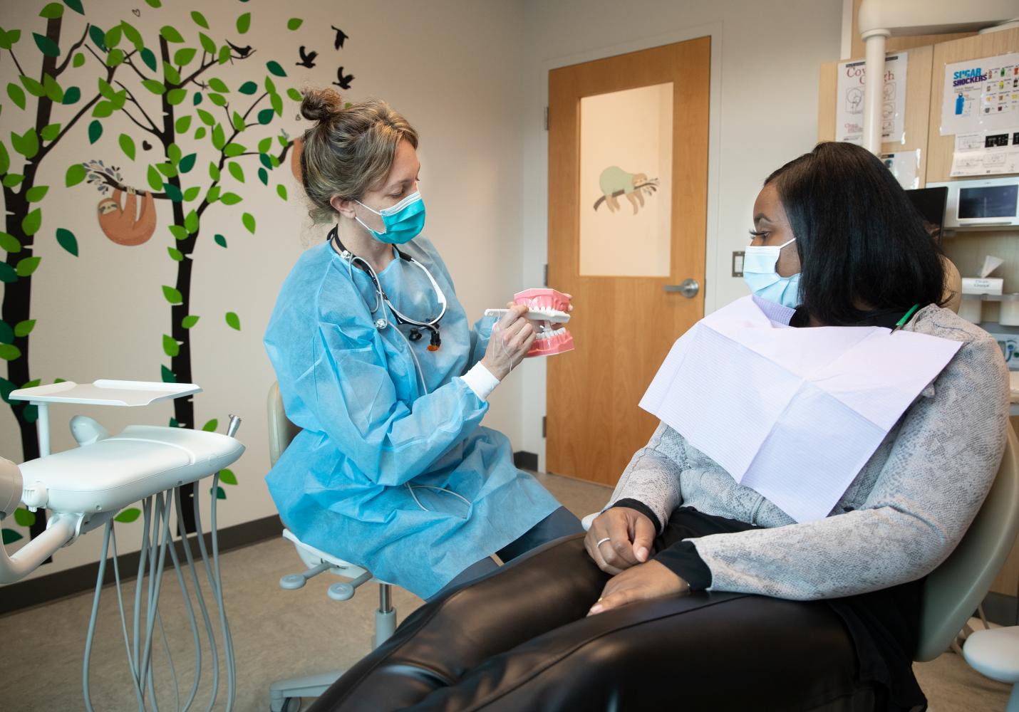 A dental team member shows a patient a model of the human mouth during a dental visit.