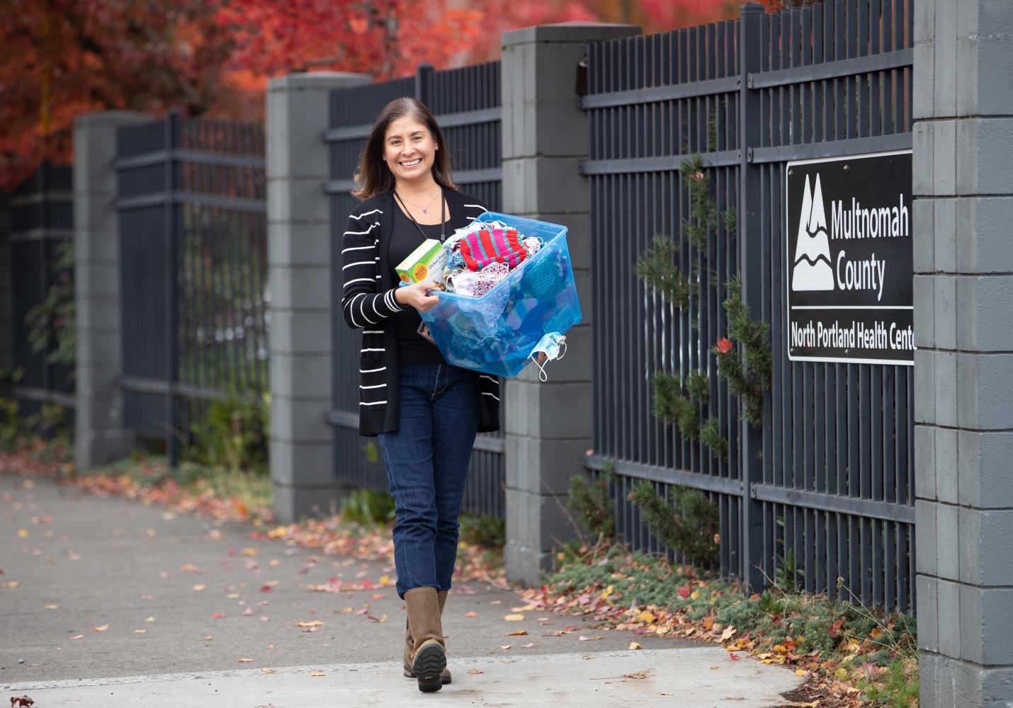 A woman stands near a North Portland Health Center sign and is holding a basket of food and clothing.