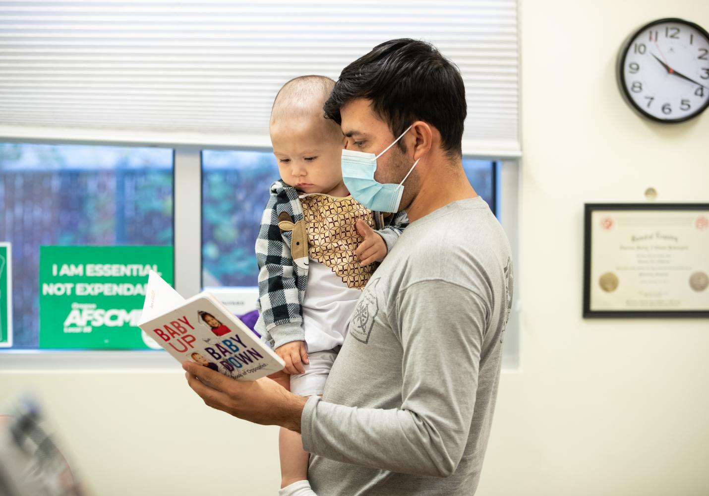 A father reads a book to a baby before a visit at a Community Health Center.