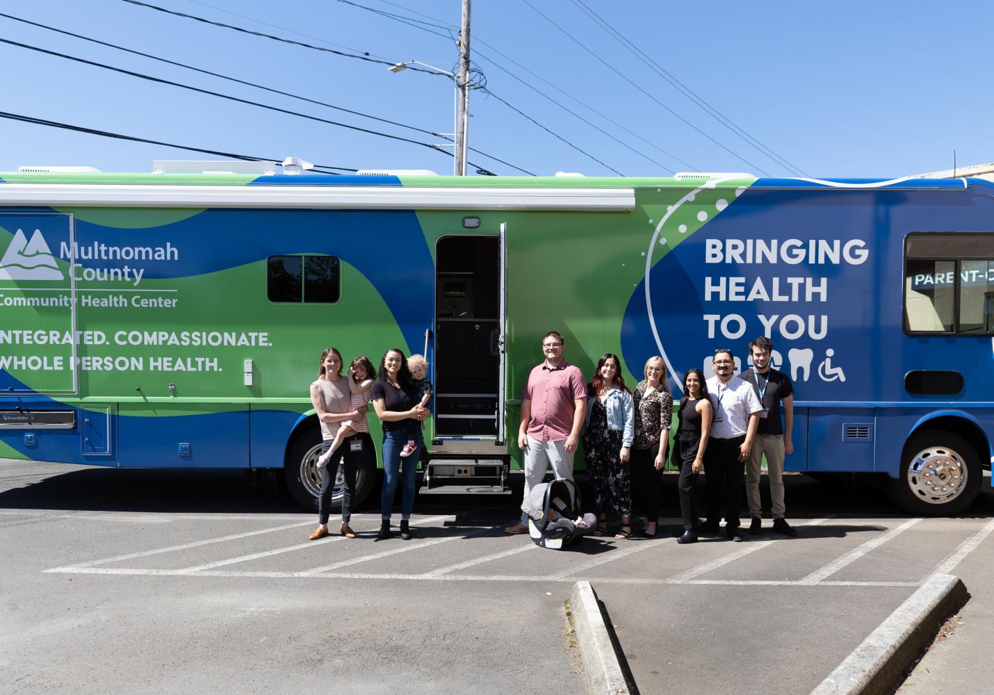 A group of people stand outside of a mobile clinic medical van. The side of the van reads Bringing Health to You.