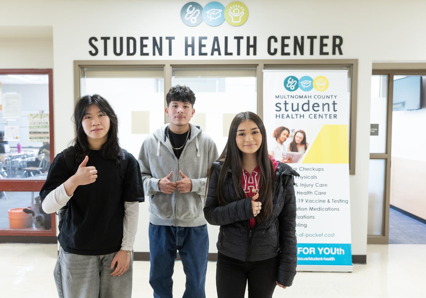 Three teenagers stand near the entrance of a Student Health Center.