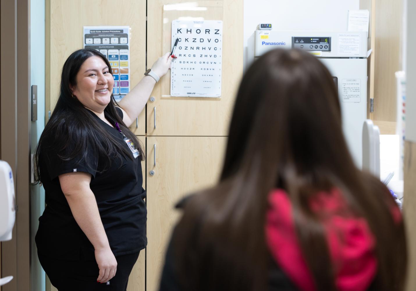 A health care team member points to letters on an eye chart during a patient visit.