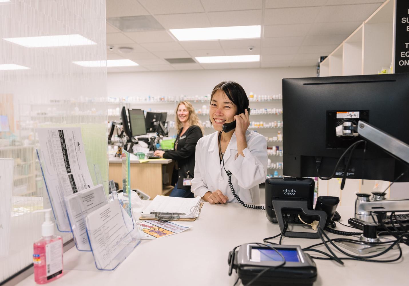 A health care team member answers a phone while sitting at a desk and smiling.