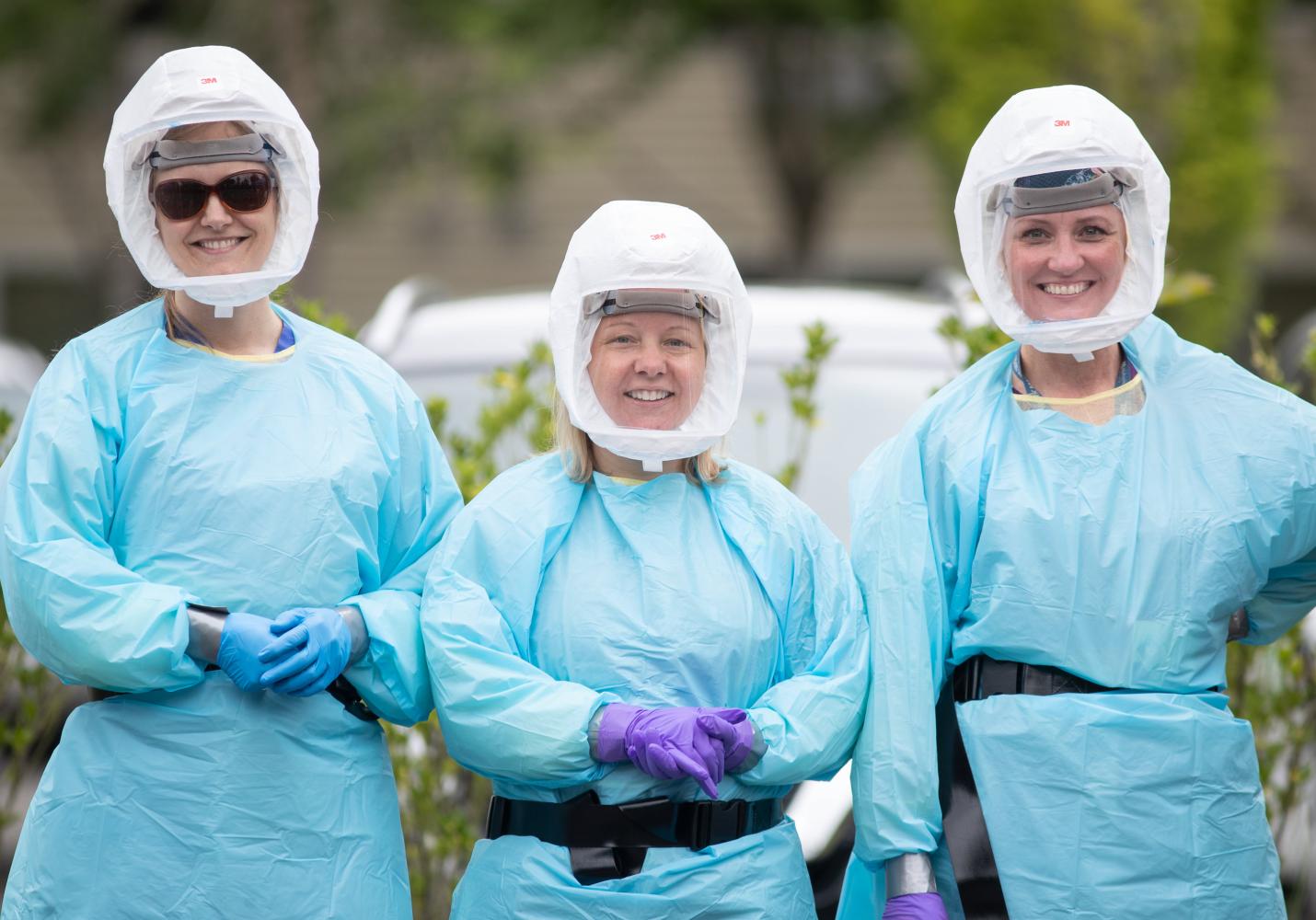 Health care team members wearing protective gear stand together smiling.