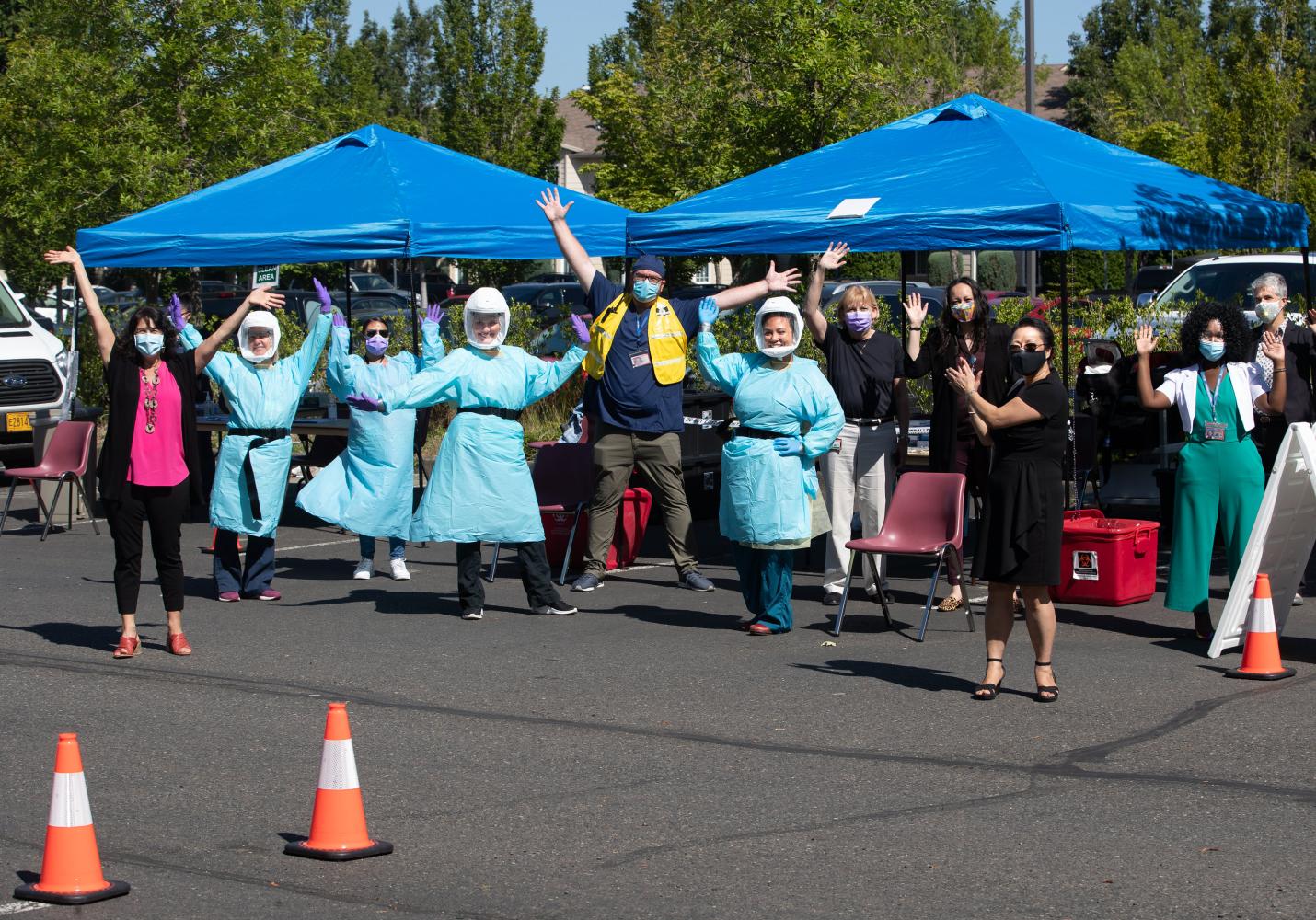 Health care team members wearing protective gear cheer at a community event.