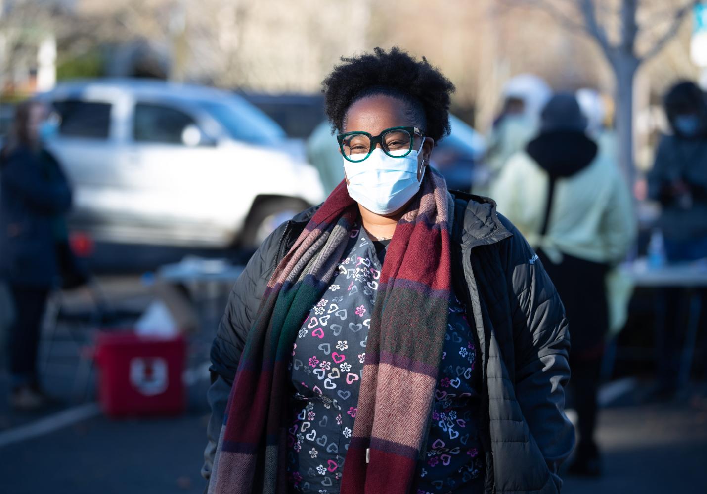 A volunteer wearing glasses and a face mask stands at a community event.