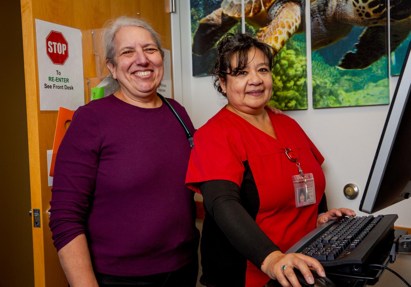 Two health care team members smile as they work together at a computer screen.