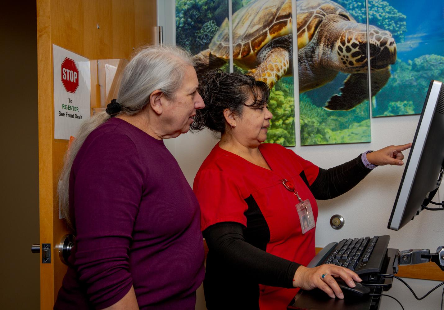 Two health care team memnbers review patient information on a screen.