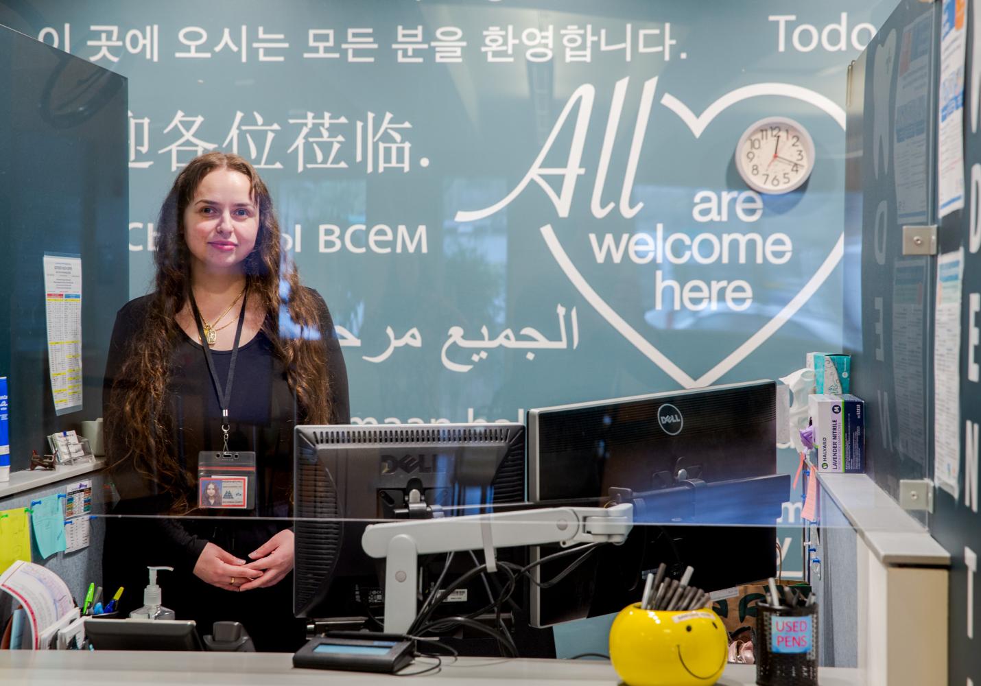 Staff person in front of front desk sign that says "All are welcome here"