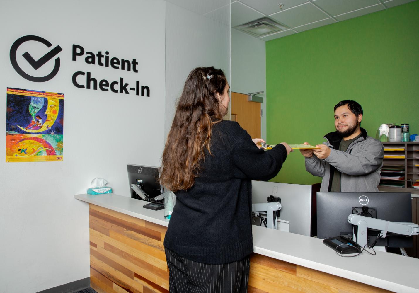 A team member hands paperwork to a patient at the front desk of a health center.