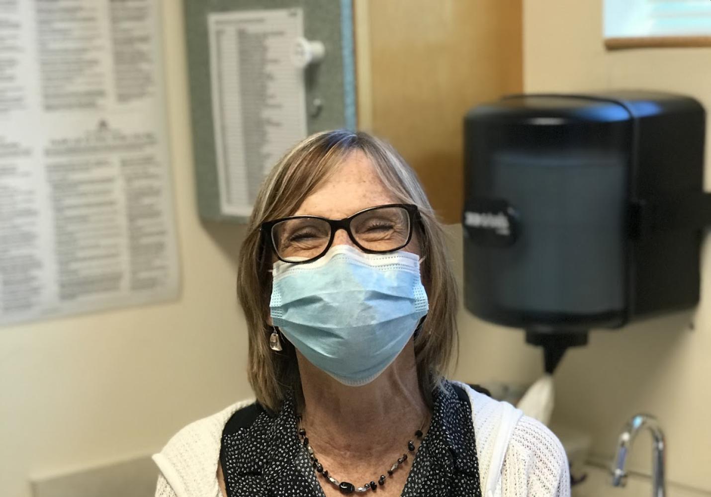 A health care team member wearing a face mask stands near a sink in an examination room.