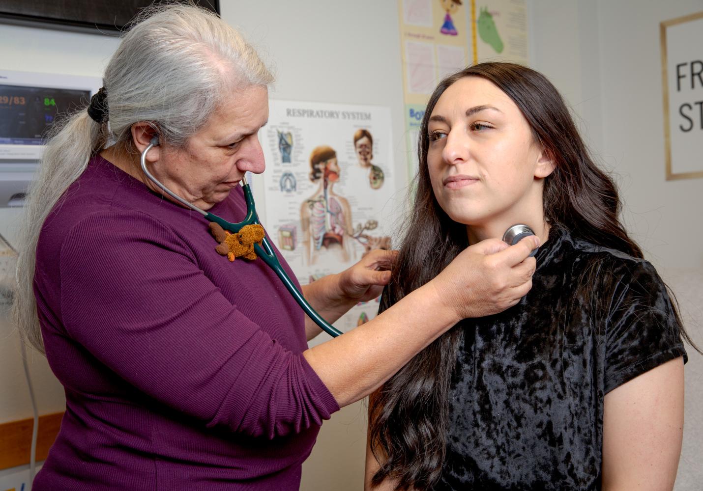 A health care team member checks a patient's vital signs with a stethoscope.