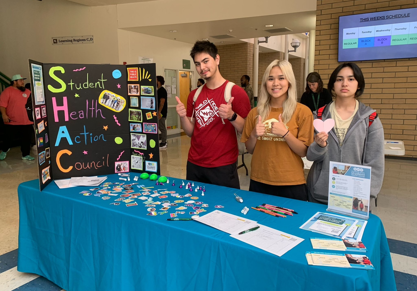 Three teenagers stand behind a table with information about their Student Health Action Council.