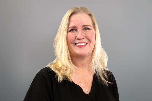 Jo Walton is dressed in a black shirt and a silver necklace and smiles in front of a grey backdrop