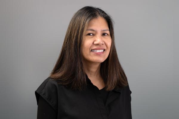 Rosebelinda Nelson is dressed in a collared black blouse and smiles in front of a grey backdrop 